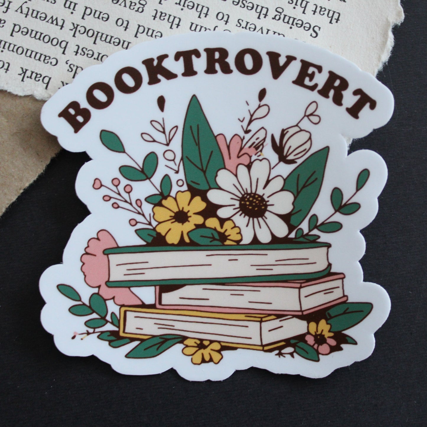 Sticker with 'Booktrovert' design featuring books and flowers on a dark background
