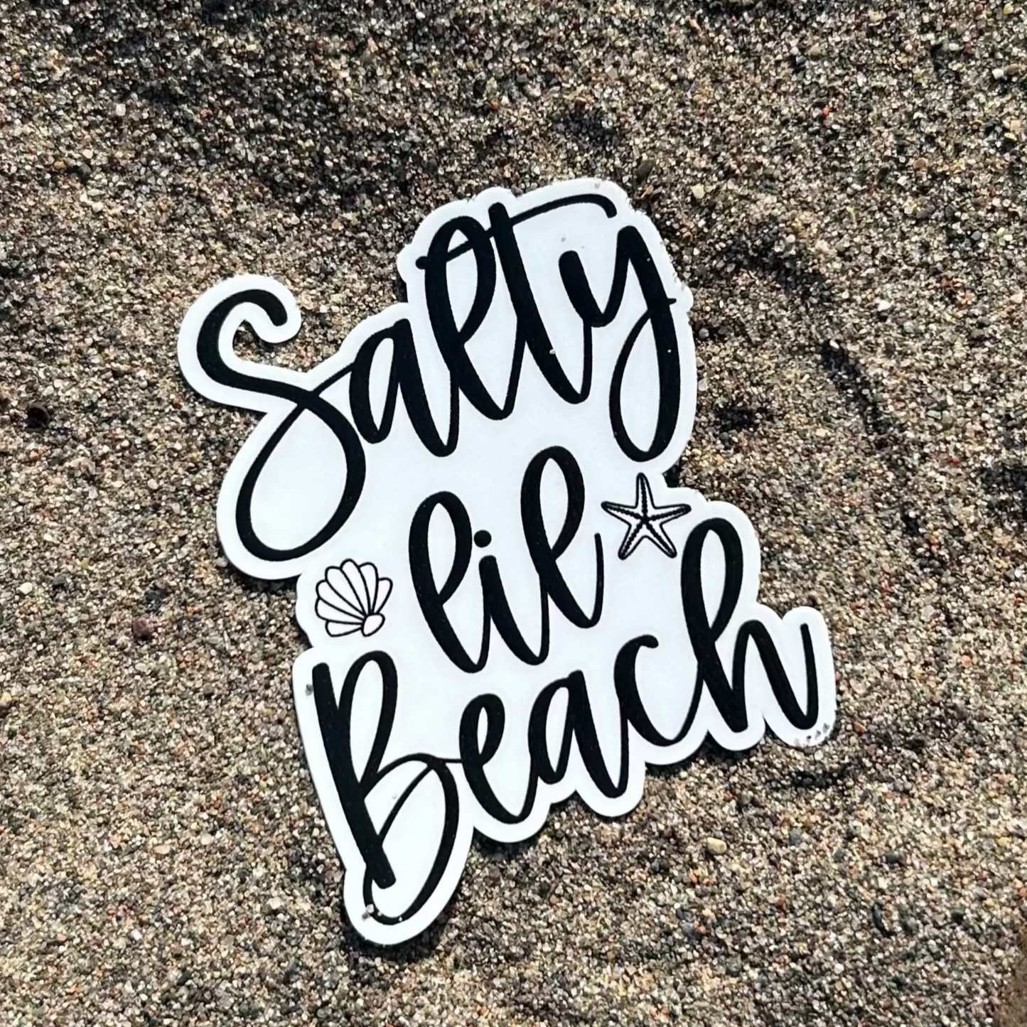 Sticker with 'Salty Lil Beach' text on sand with rocks